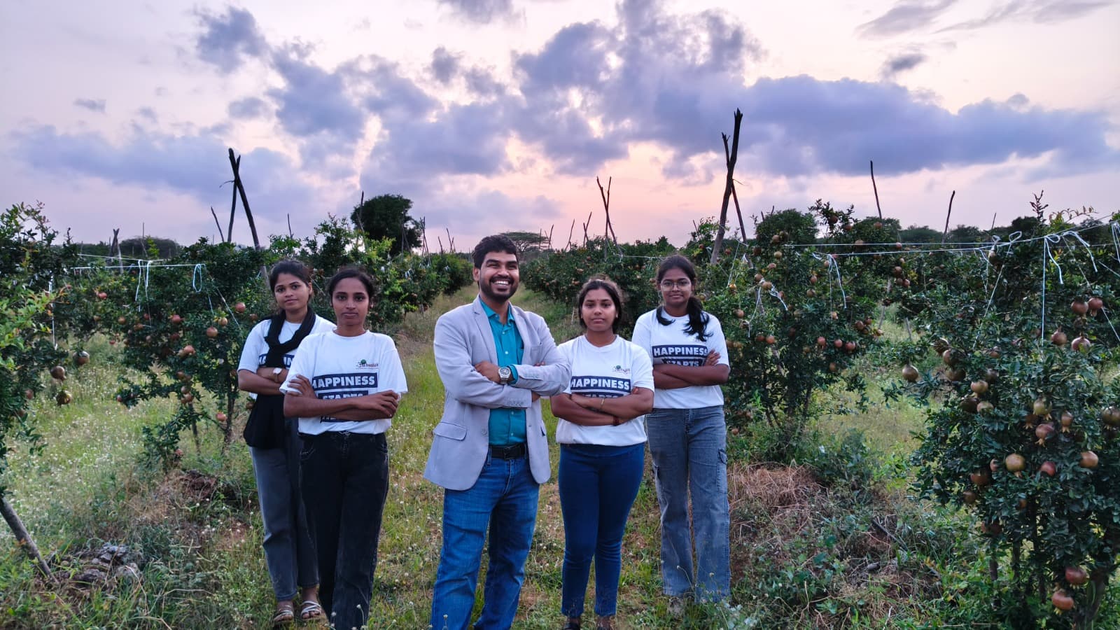 Aahwahan volunteers and the founder standing together in a pomegranate orchard at dusk